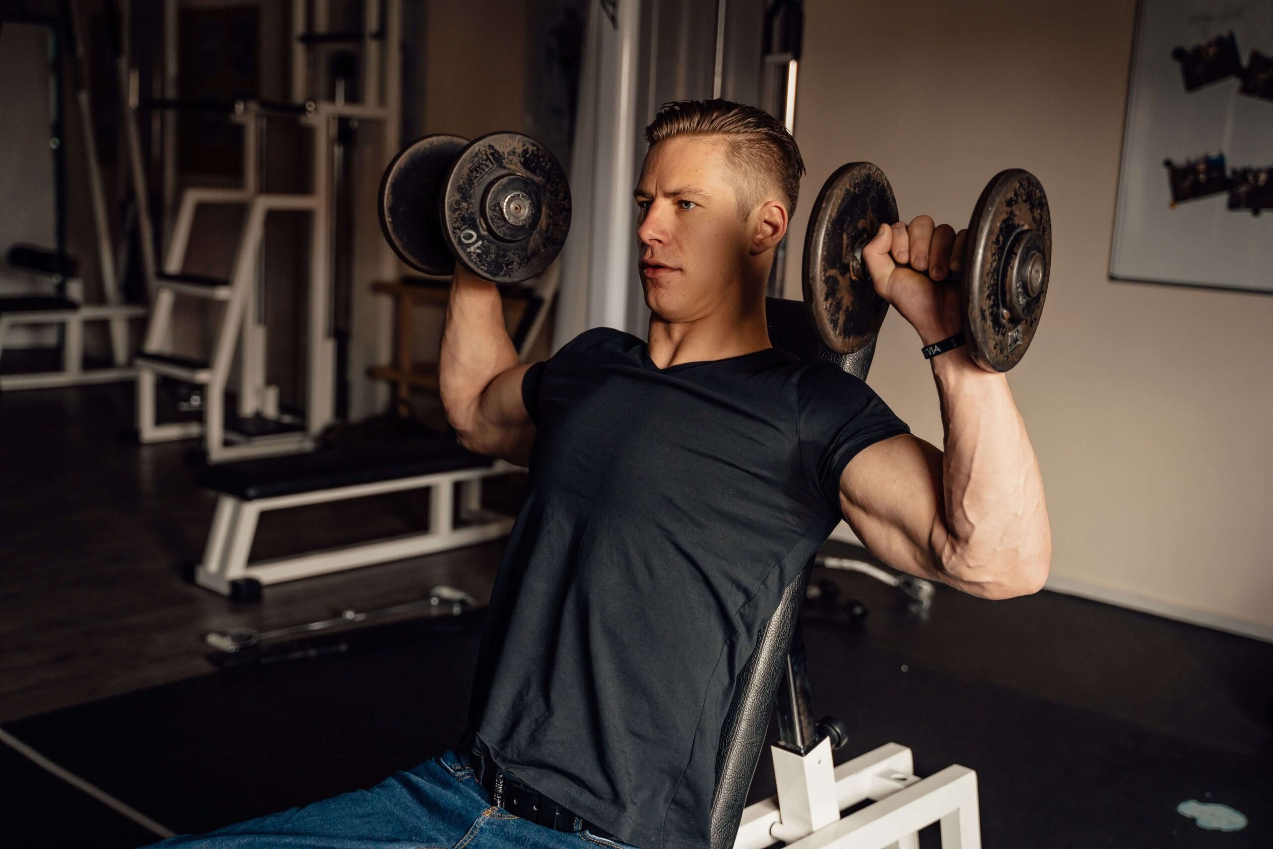 Man performing a dumbbell bench press on a flat bench in a gym, focused on chest and shoulder strength training