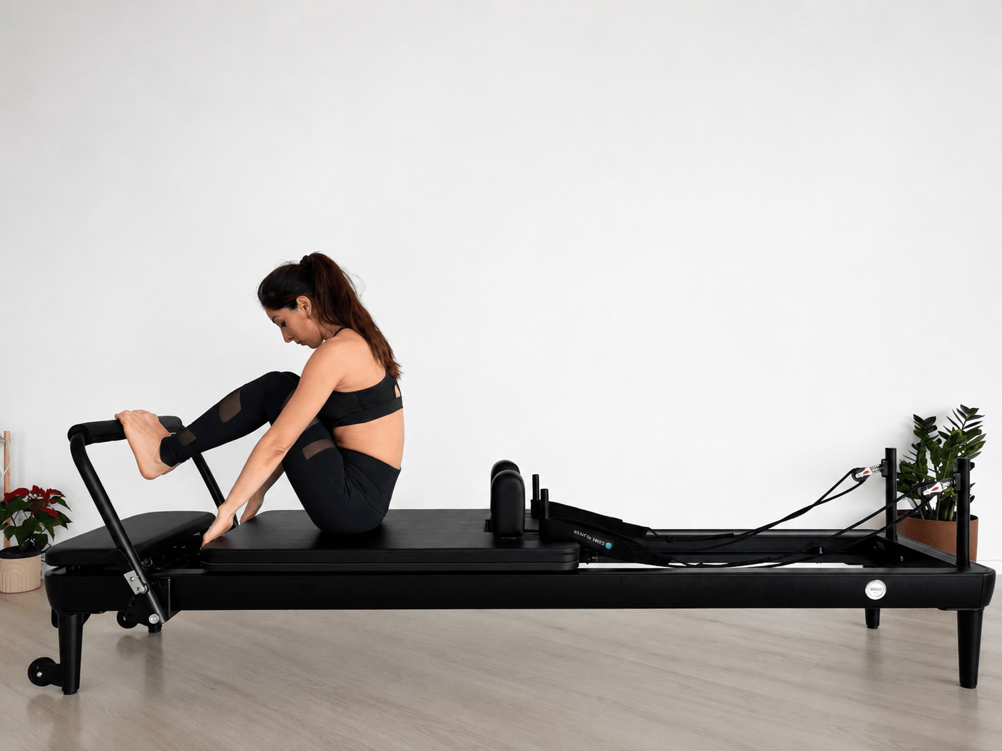 Woman performing an advanced pilates reformer workout with increased spring resistance in a bright studio