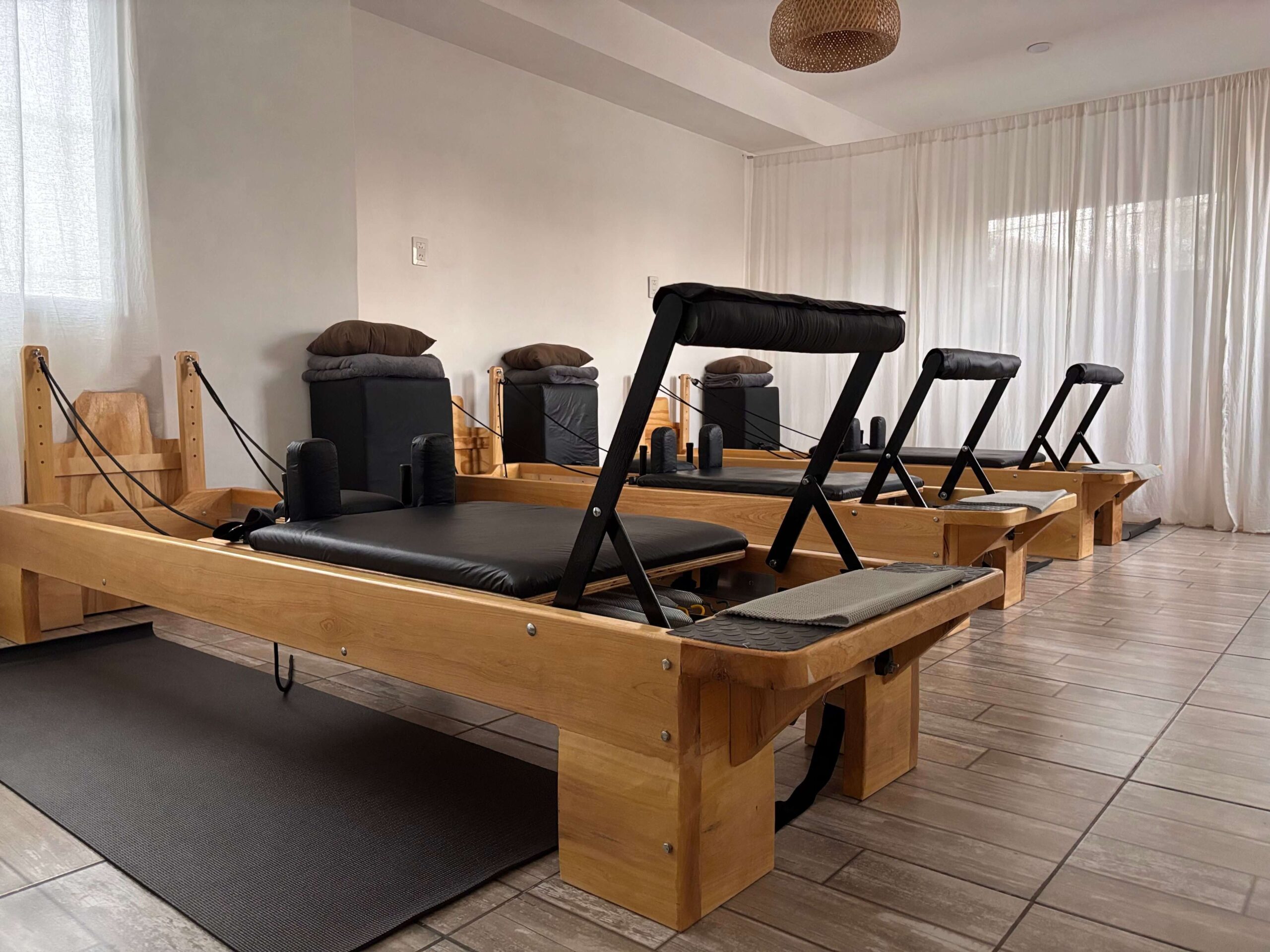 Wooden pilates reformer workout machine with visible resistance springs in a bright, modern studio